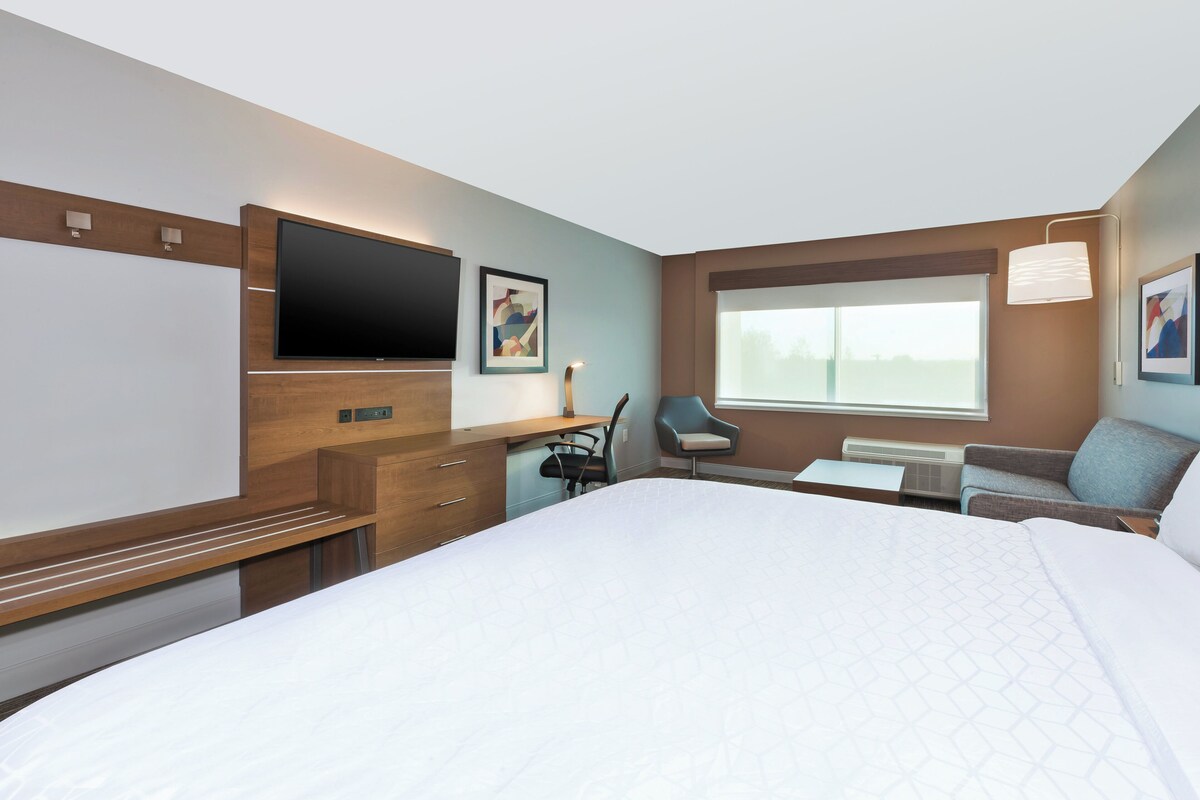 Quarto de hotel com cama, escrivaninha, cadeira, televisão e janela.