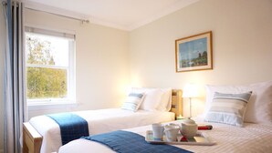 Hotelkamer met twee bedden, een raam met gordijnen, een schilderij aan de muur, en een dienblad met kopjes en een boek op het bed.