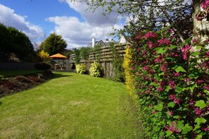 Ein gepflegter Garten mit Holzzaun, einer Holzpergola und blühenden Pflanzen.