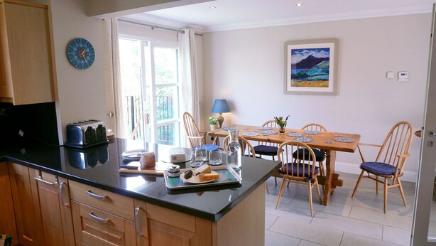 Een moderne keuken met een centraal eiland, houten kastjes en een eethoek met een tafel gedekt voor vier personen.