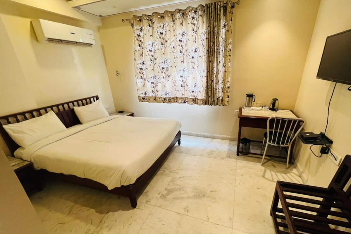 Una habitación de hotel con cama, escritorio, silla, televisor y aire acondicionado.