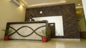 Un mostrador de recepción con una pared de mármol, un reloj y dos plantas en macetas.