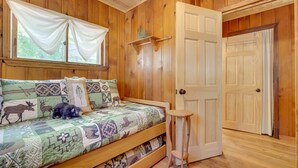 Quarto de cabana de madeira com cama, uma mesa pequena e uma porta.