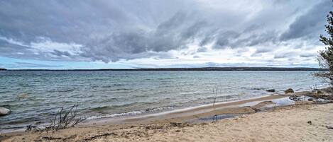 Una platja amb sorra, aigua tranquil·la i cel nuvolós.