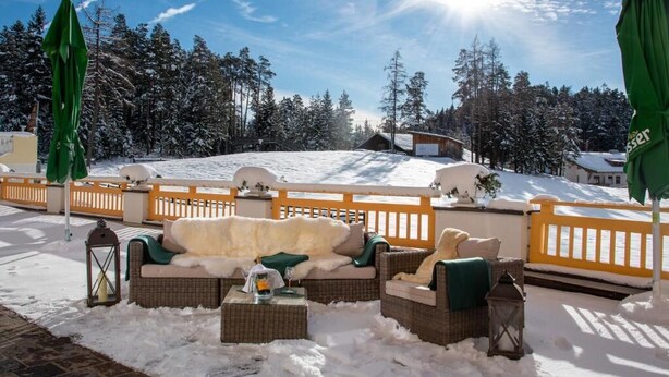 Un espace extérieur aménagé avec des meubles en osier, recouvert de neige, et offrant une vue sur un paysage enneigé et des arbres.