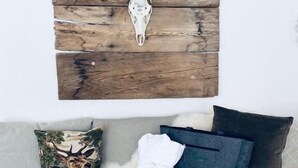 Une pièce décorée d’une œuvre d’art murale en bois représentant un crâne de cerf, d’un tapis en fausse fourrure moelleuse, d’un coussin orné d’un motif de cerf et de serviettes blanches soigneusement pliées.