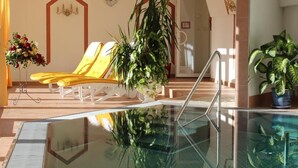 Un hall d’hôtel avec une piscine entourée de parois en verre, des fauteuils de couleur jaune et des plantes en pot.