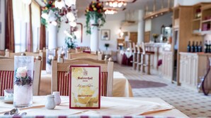 Une scène de restaurant avec une table dressée pour le dîner, comprenant un menu, des salières et des poivrières, ainsi qu’un arrangement floral décoratif.