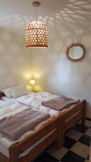 A bedroom with a wooden bed, a patterned hanging light fixture, a bedside table with a lamp, and a round mirror on the wall. - Europa Feriendorf (Lichtenau)