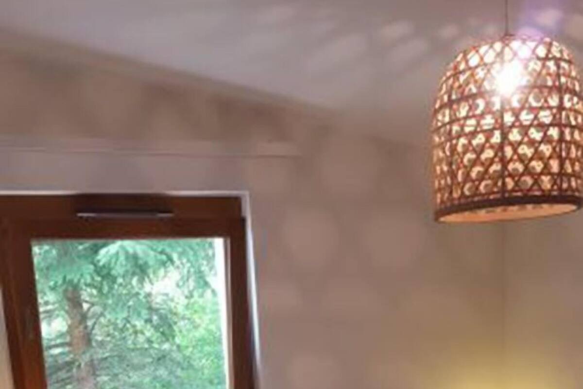 A bedroom with two beds, a window, a hanging light fixture, and a nightstand with a lamp.