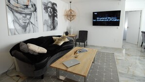 A modern living room with a black leather sofa, a wooden coffee table with a laptop, and a TV on the wall displaying 'Airplane Repo Inkasso-Pilote'. - White House Puerto Banus (Nueva Andalucía)