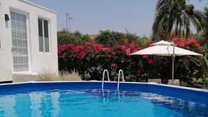 A clear blue swimming pool with a white poolside umbrella, surrounded by lush greenery and pink flowers. - White House Puerto Banus (Nueva Andalucía)
