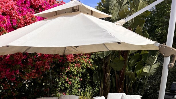 A patio with a glass coffee table, white cushioned sofas, and a large umbrella. - White House Puerto Banus (Nueva Andalucía)