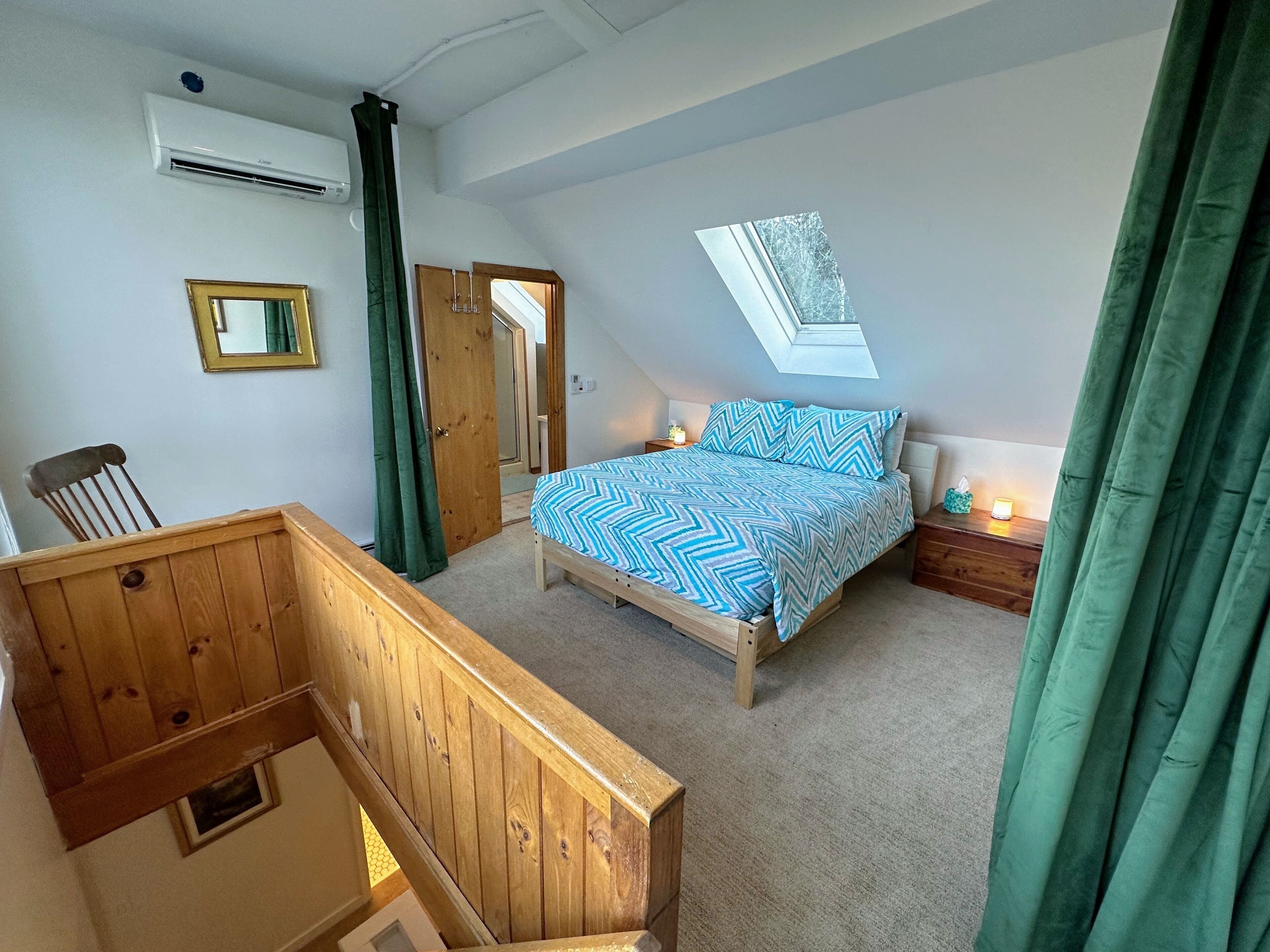 A bedroom with a bed, a wooden chair, a nightstand, a mirror, and a skylight.