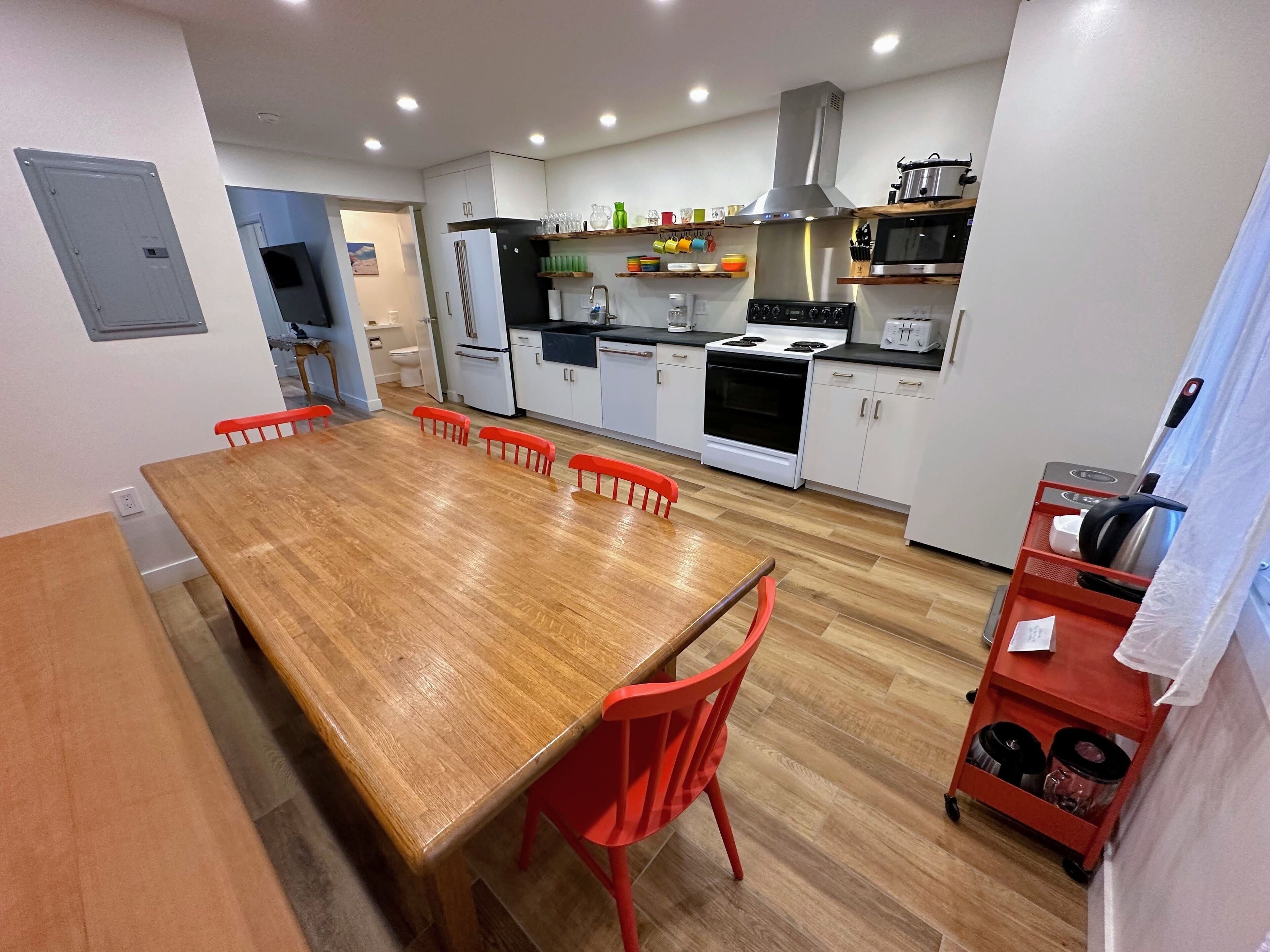 Una cocina moderna con armarios blancos, una mesa de comedor de madera, sillas rojas y un carrito de cocina rojo.