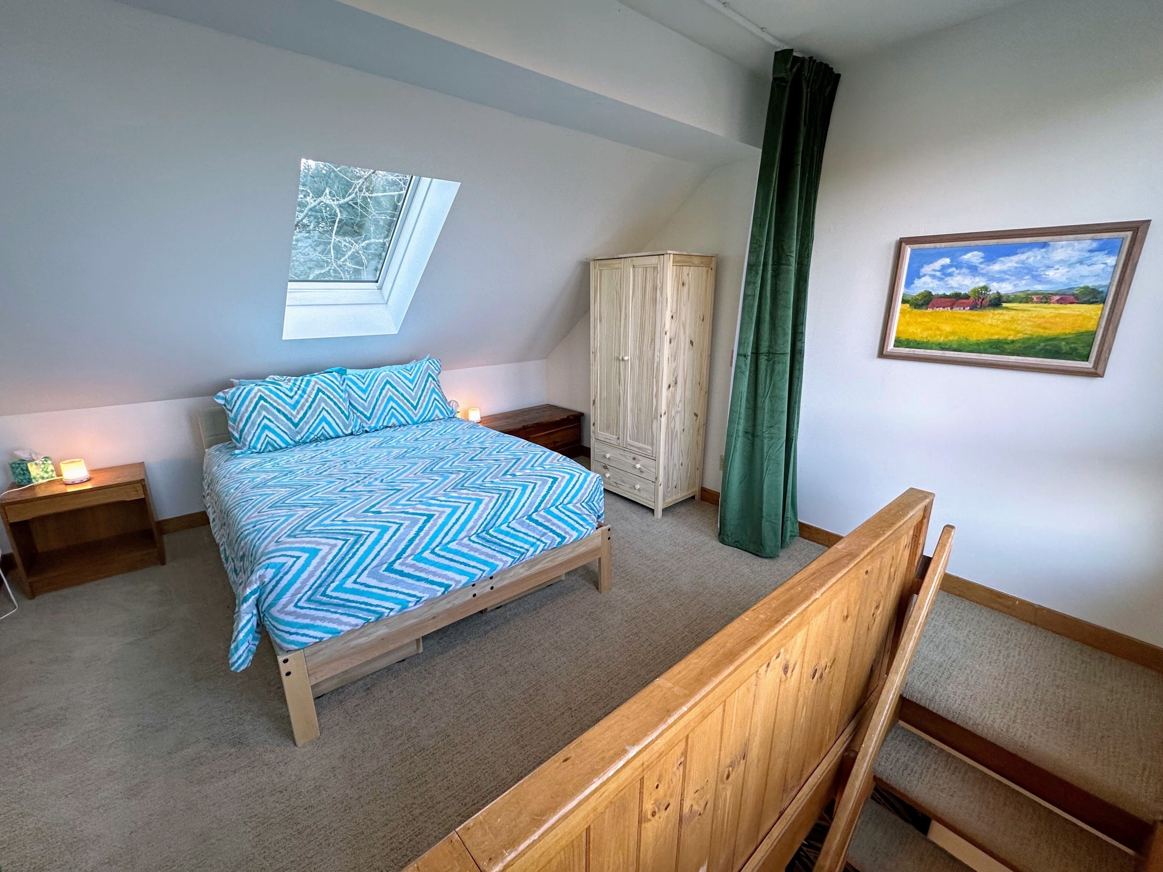 Un dormitorio con cama, mesita de noche, armario, ventana y cortina verde, además de un cuadro de paisaje en la pared.