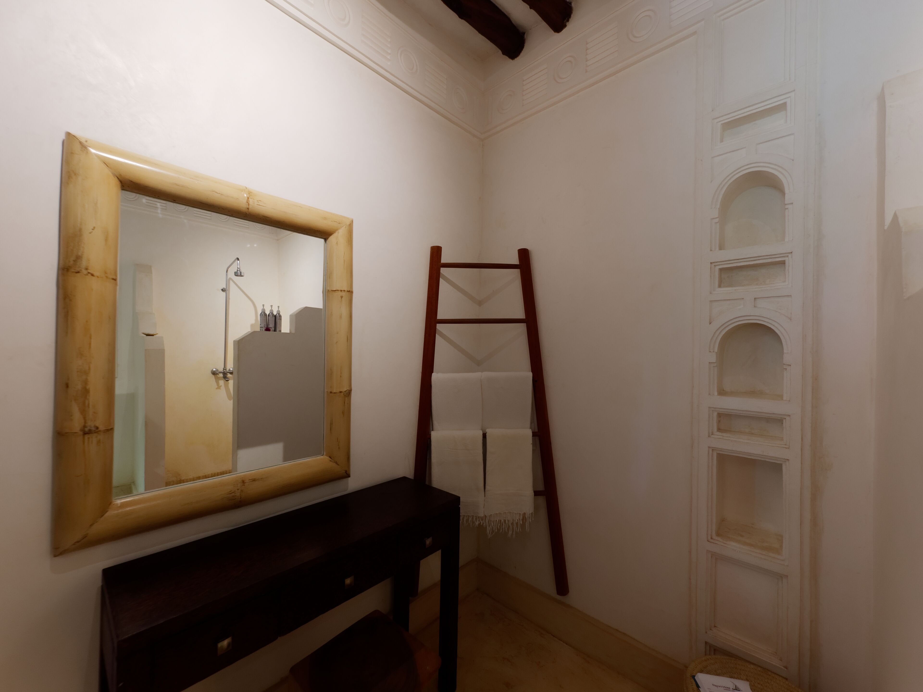 A bathroom with a wooden vanity, a mirror, a shower, and a wooden ladder leaning against the wall.