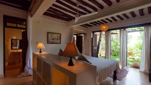 A bedroom with a bed, bedside lamps, a painting, and a view of the garden. - Peponi Hotel (Lamu)