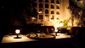 A dimly lit dining area with a table set for two, surrounded by ornate wall decorations and a large tree. - Peponi Hotel (Lamu)