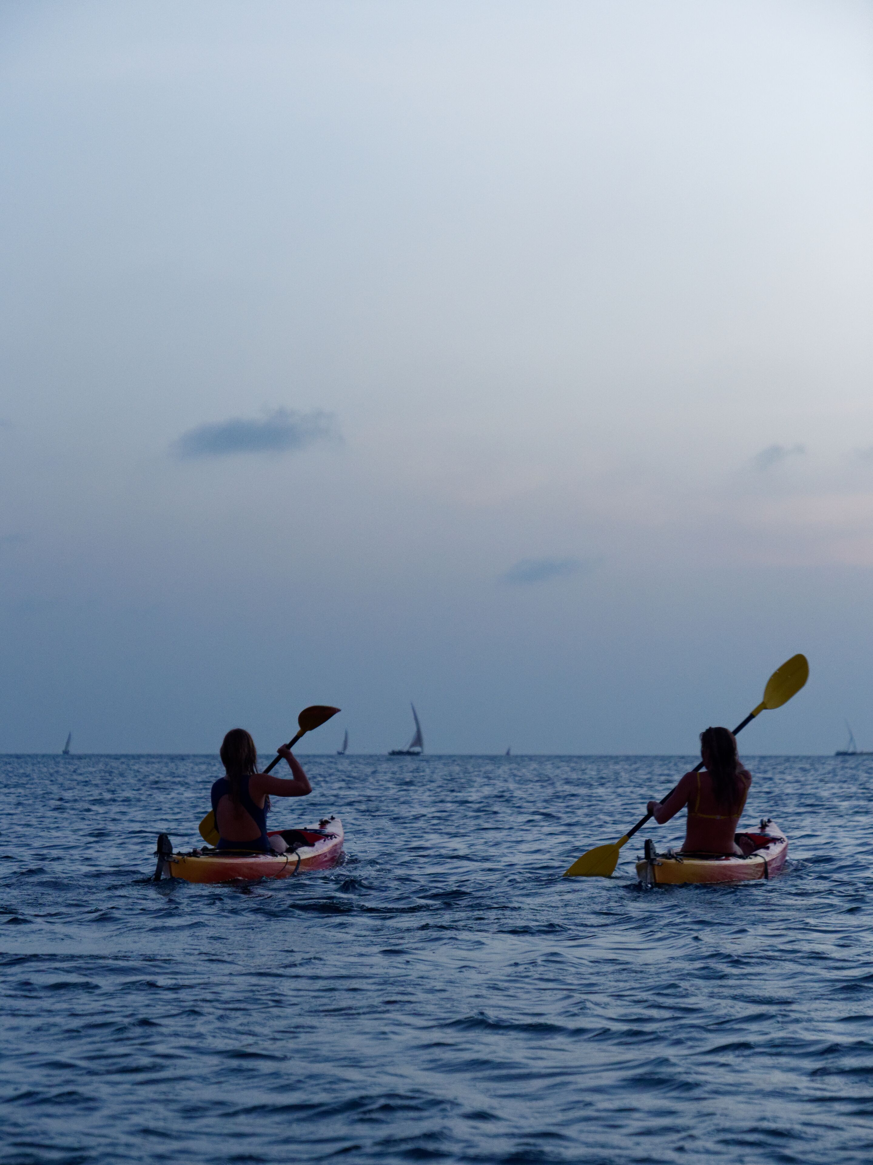 Two kayaks on calm water with a distant sailboat.