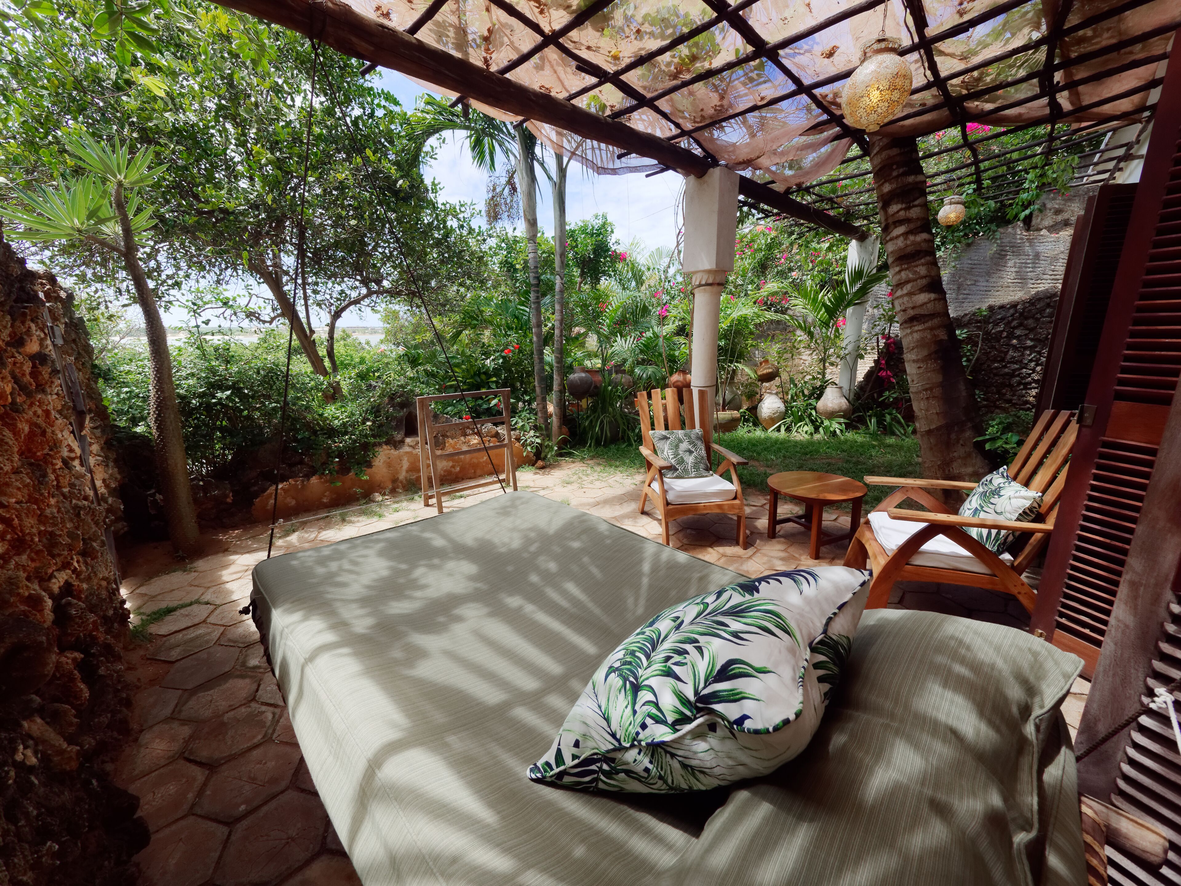 A covered outdoor seating area with a cushioned bench, wooden chairs, and a small table.