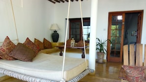 A cozy room with a hanging swing bed, a sofa with patterned cushions, a wooden chair, a potted plant, and a lamp. - Peponi Hotel (Lamu)