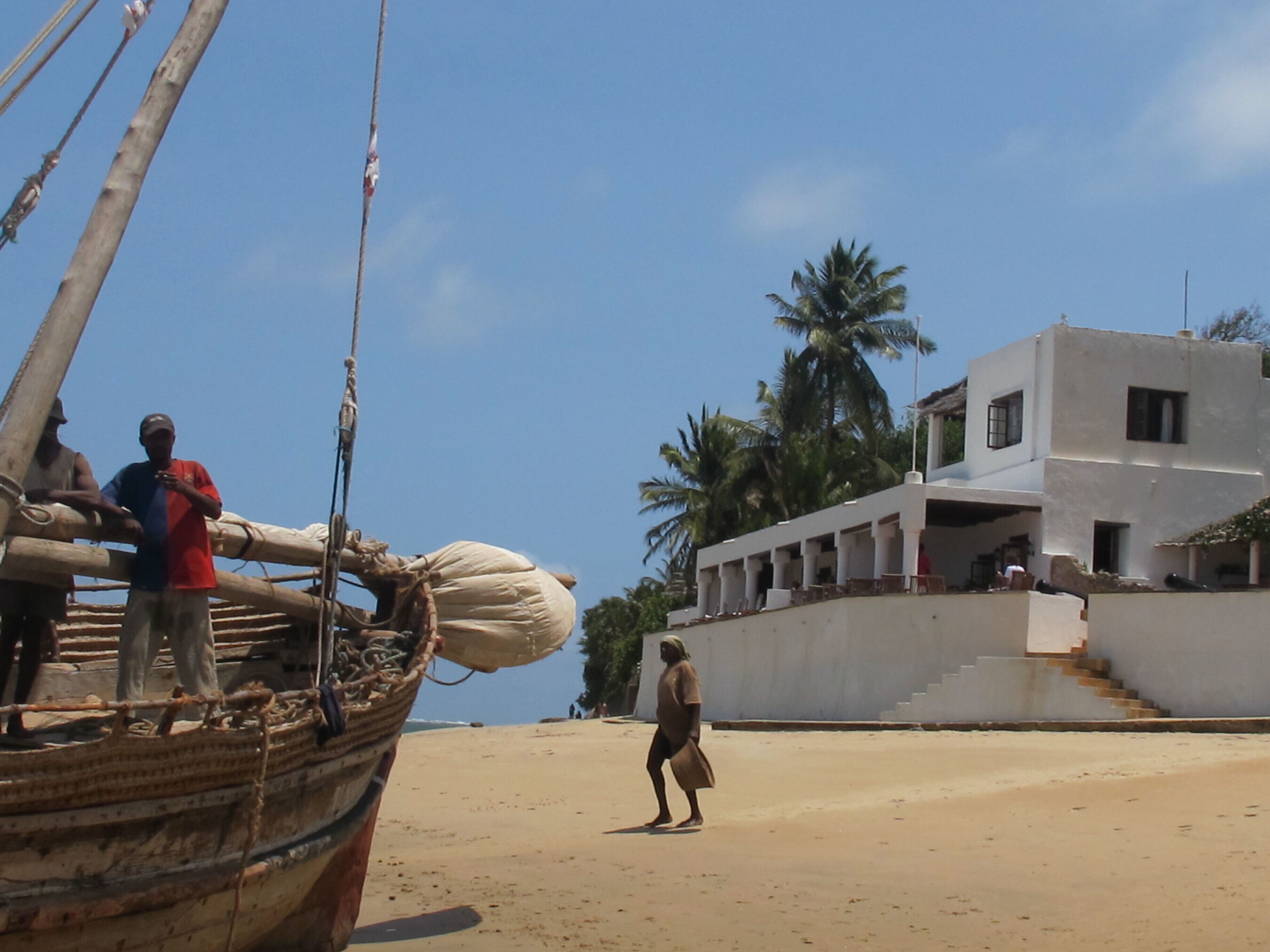 Una playa con un bote, un edificio con escalones y palmeras.