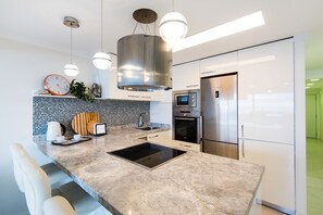 A modern kitchen with a marble countertop, built-in oven, microwave, and stainless steel refrigerator.