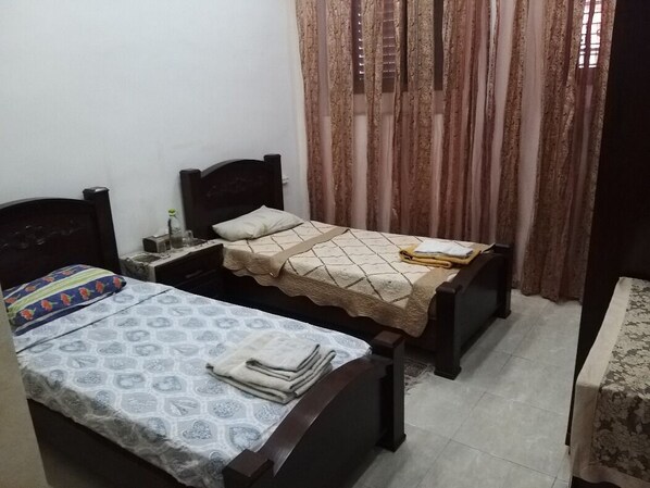 A small bedroom with two single beds, a nightstand, and a table with a tablecloth.