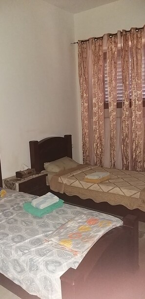 A bedroom with two beds, a nightstand, and a window with curtains.