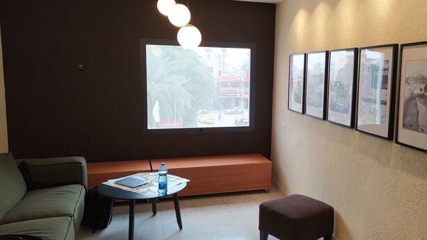 Ein modernes Zimmer mit großem Fenster, einer Couch, einem kleinen Tisch mit einer Wasserflasche und gerahmten Bildern an der Wand.