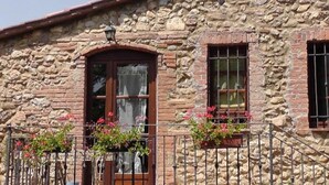 A stone building with a wooden door and windows, a balcony with metal railings, and potted plants with red flowers. - Agriturismo Il Poderino (Bibbona)