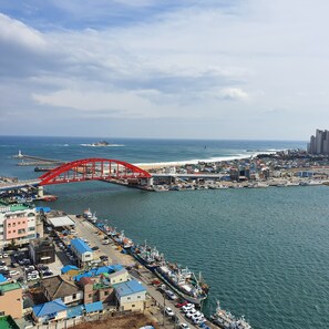 A coastal cityscape with a prominent red bridge, a marina with boats, and a lighthouse in the distance. - SOTA SUITE SOKCHO WORLDSTATE (Sokcho)