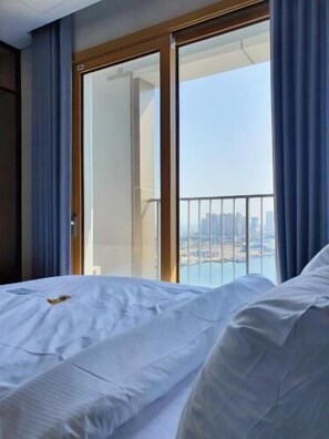 A hotel room with a bed, a view of the city through a balcony, and a sliding door. - SOTA SUITE SOKCHO WORLDSTATE (Sokcho)