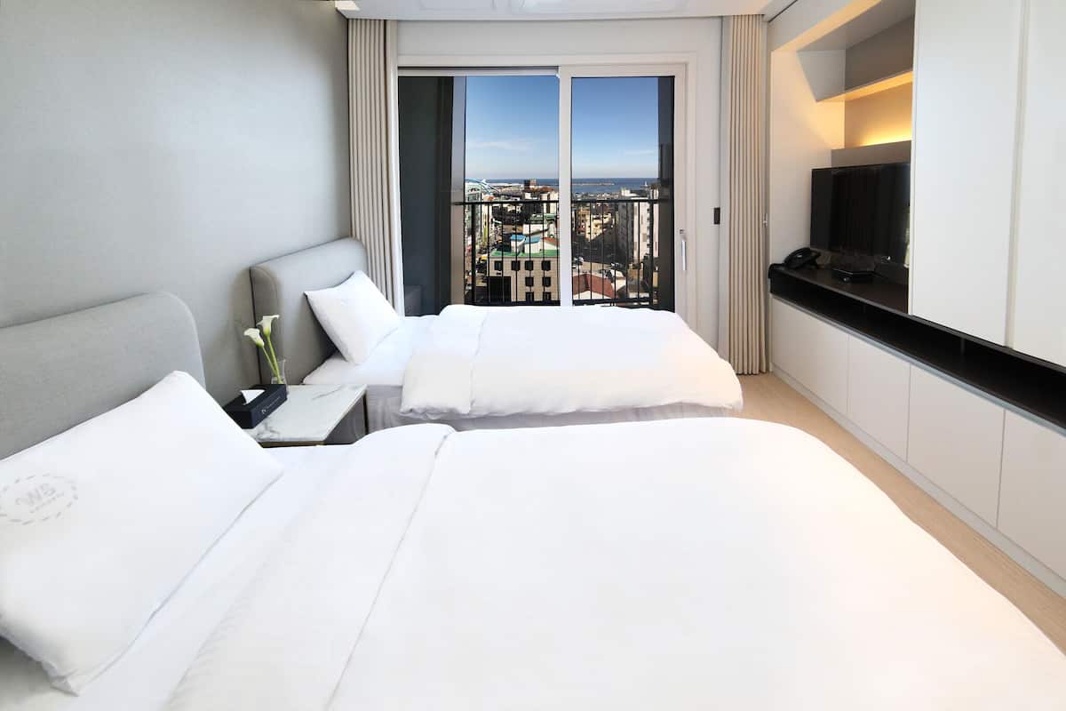 A hotel room with two beds, a TV, and a balcony with a city view.