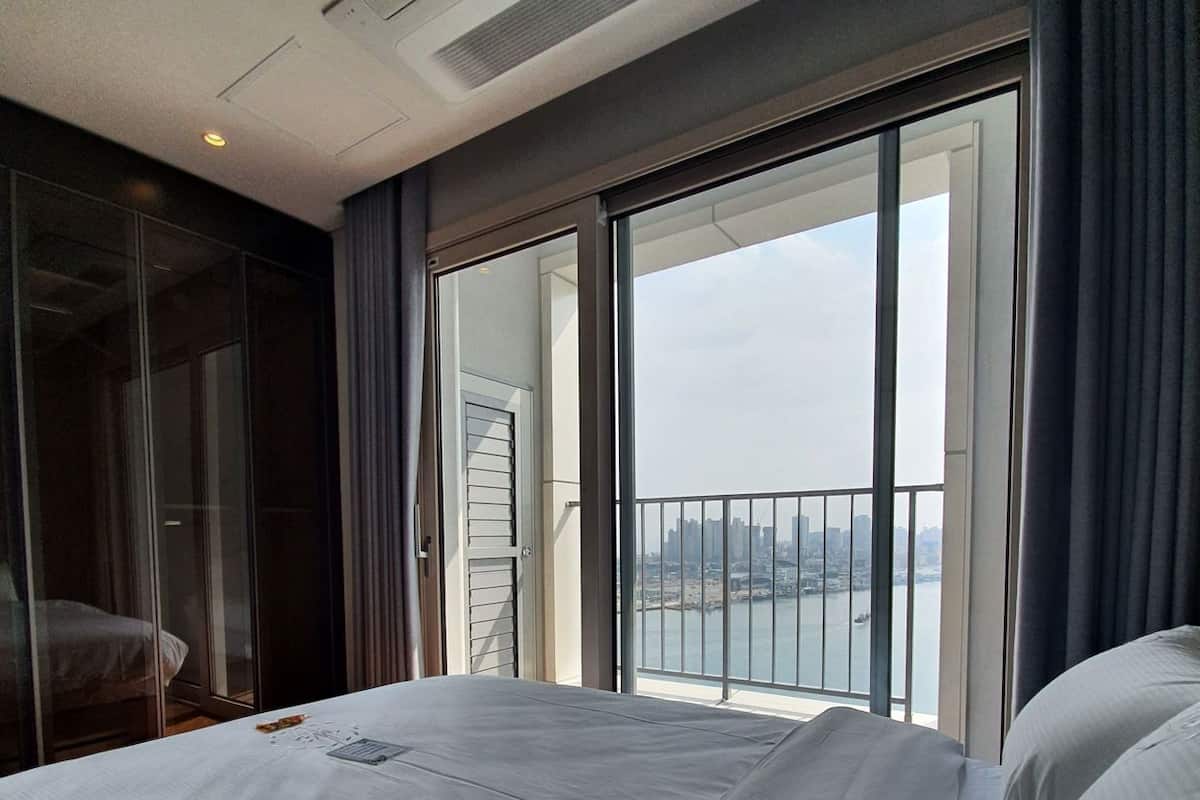 A hotel room with a bed, a sliding glass door to a balcony, and a view of a cityscape.