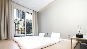 Une chambre d’hôtel moderne avec un grand lit, une vue sur la ville grâce à de grandes fenêtres du sol au plafond, et une petite table de chevet agrémentée d’un vase de fleurs.