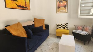 A living room with a dark blue sofa, a yellow ottoman, a white coffee table, and two framed pictures on the wall.