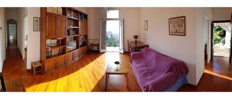 A spacious living room with a wooden bookshelf, a purple sofa, and a view of the outdoors through a large window.