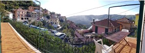 A residential area with a view of a valley, houses with red roofs, and parked cars.