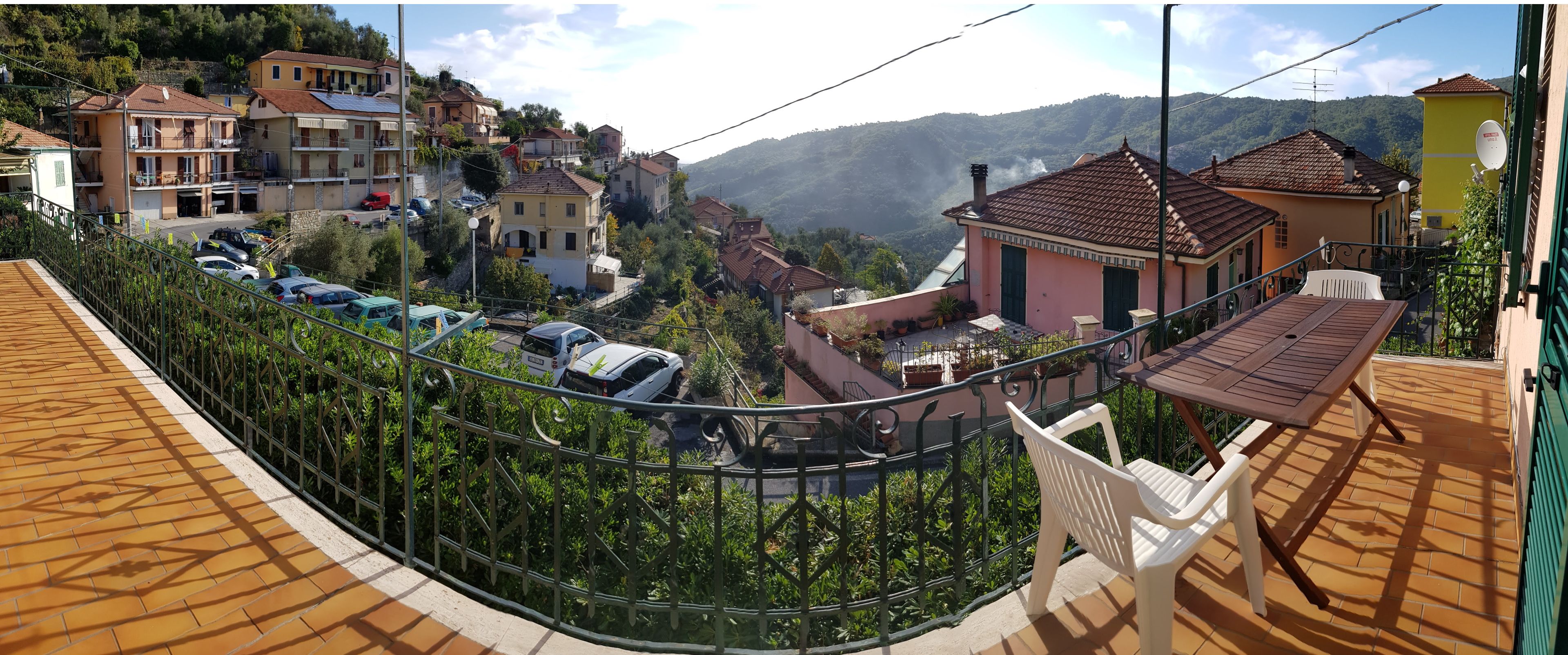 A residential area with a view of a hillside, houses with red-tiled roofs, and parked cars.