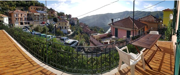 A residential area with a view of a hillside, houses with red-tiled roofs, and parked cars.