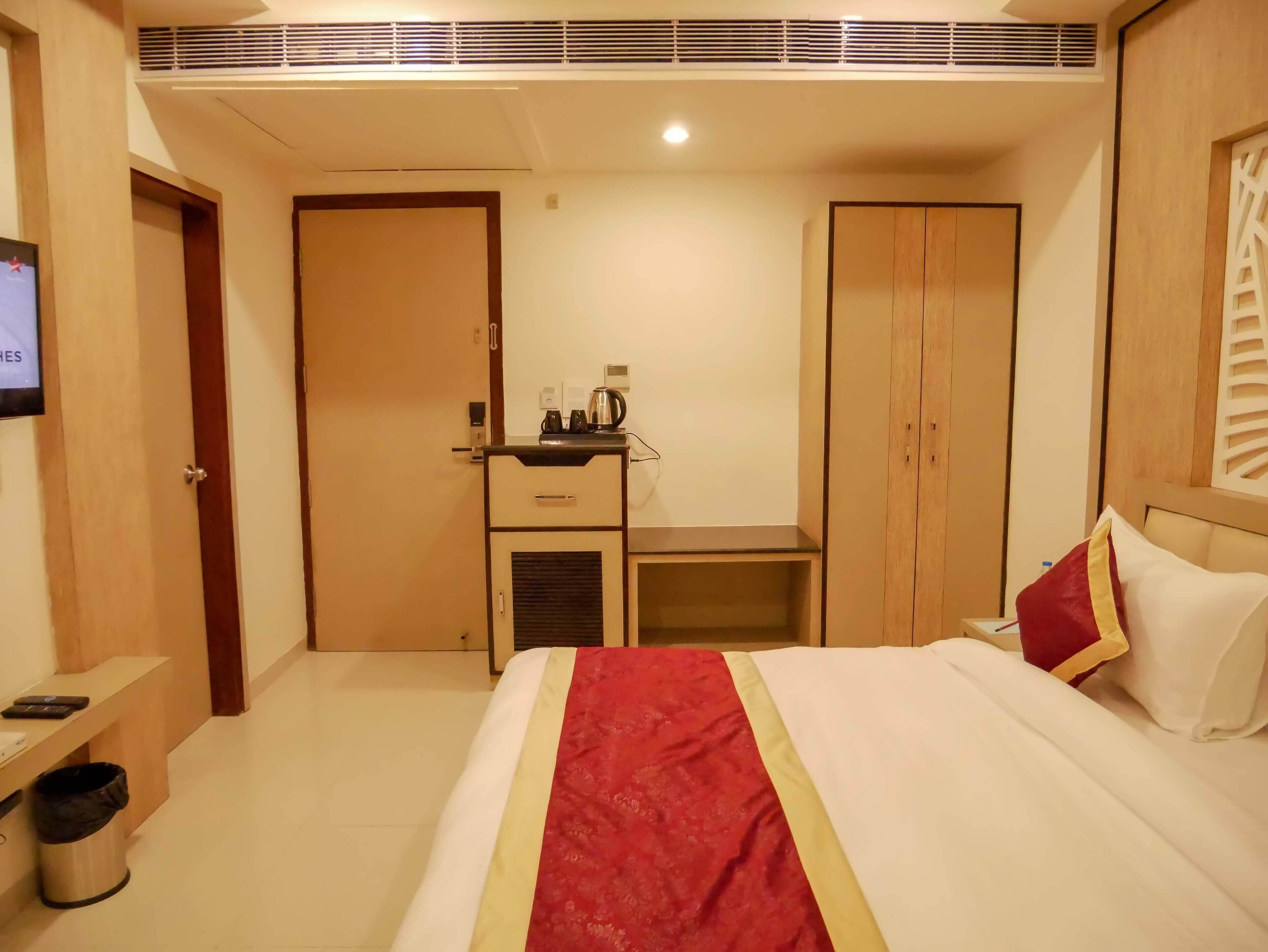 A hotel room with a bed, a desk, a wardrobe, and a television on the wall.