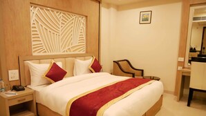 Ein Hotelzimmer mit einem großen Bett, einem hölzernen Kopfteil, einem Nachttisch mit Telefon und einem Glas Wasser, einem Schreibtisch mit Stuhl und einem Spiegel.