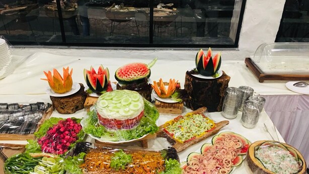 Ein Buffet mit verschiedenen Speisen, darunter eine Wassermelone als Mittelpunkt, Salaten und weiteren kulinarischen Köstlichkeiten.