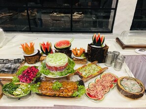 Ein Buffet mit verschiedenen Speisen, darunter eine Wassermelone als Mittelpunkt, Salaten und weiteren kulinarischen Köstlichkeiten.