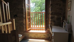 A rustic room with a wooden bench, a small table, and a window with a view of greenery outside. - La Cousteto accommodation in a 17th century fortified house (Roquefixade)