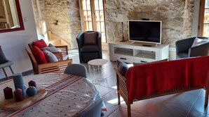 A cozy living room with stone walls, a TV, and comfortable seating. - La Cousteto accommodation in a 17th century fortified house (Roquefixade)