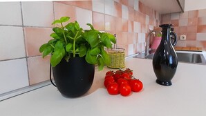 Una encimera de cocina con una planta en maceta, una cesta, una jarrón y un racimo de tomates.
