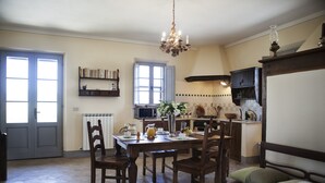 Un comedor con mesa de madera, sillas y una araña. También hay una cocina con armarios y un microondas.